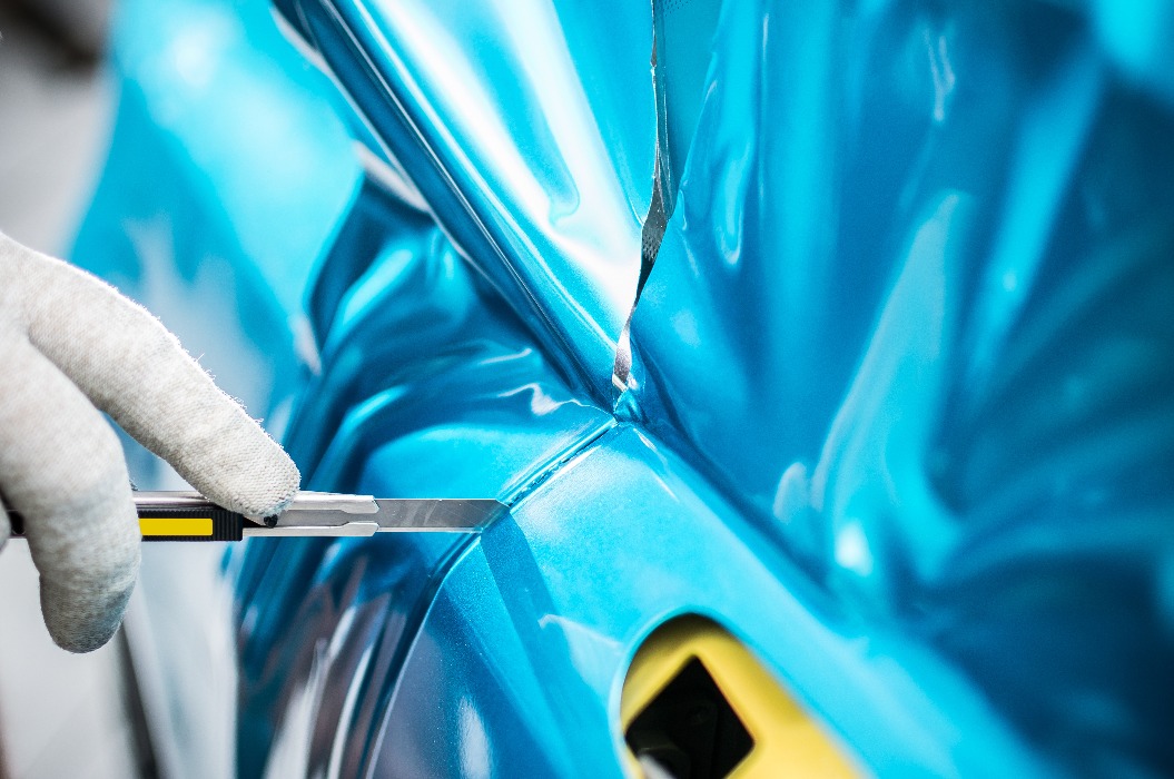 Eine Person mit Handschuh schneidet glänzende blaue Autofolie mit einem Cutter