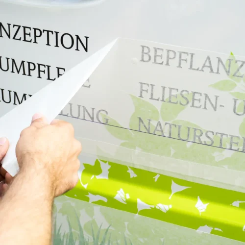 Haende  loesen  Folie,  schwarze  Beschriftung  und  gruenes  Blattmotiv  auf  Glas